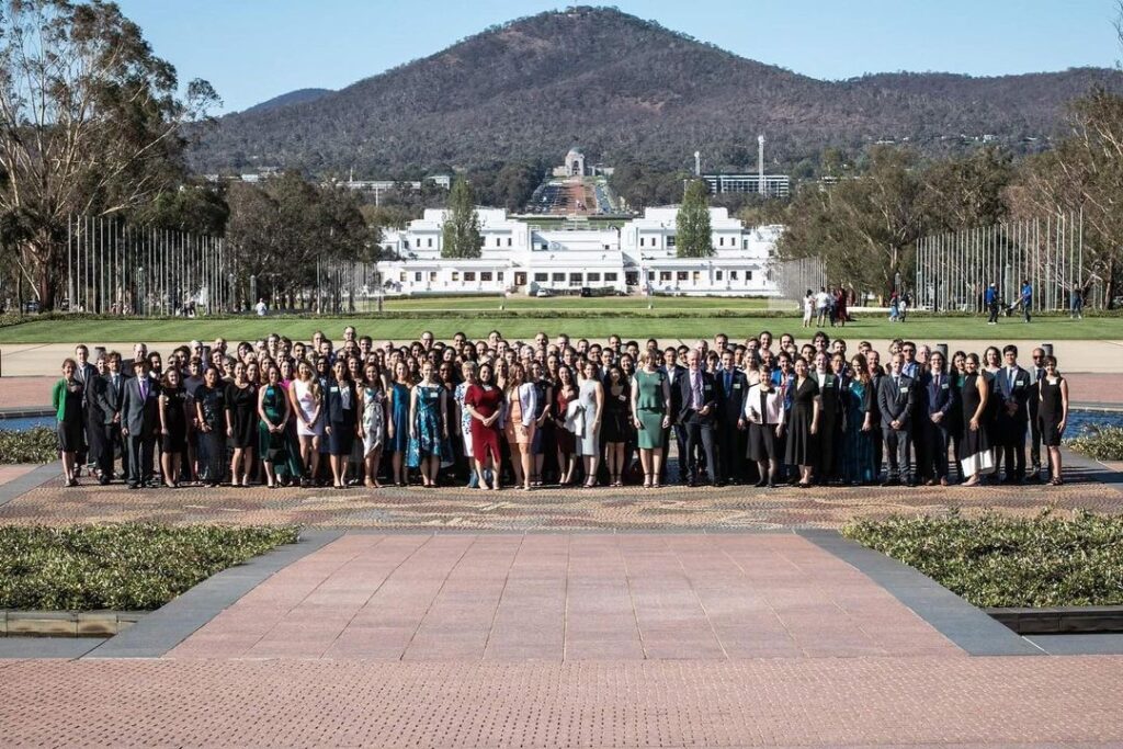 Over 100 Fulbrighters stand together in a group photo outside the Parliament House in Canberra, Australia.
