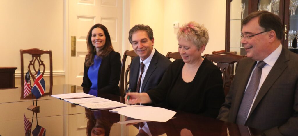 Four people sitting at a table. A woman with short, cropped blonde hair is signing an agreement between the Fulbright Commission in Iceland and the National Science Foundation. Also present are the Ambassador of Iceland to the U.S. and then-Assistant Secretary for Educational and Cultural Affairs Evan Ryan.
