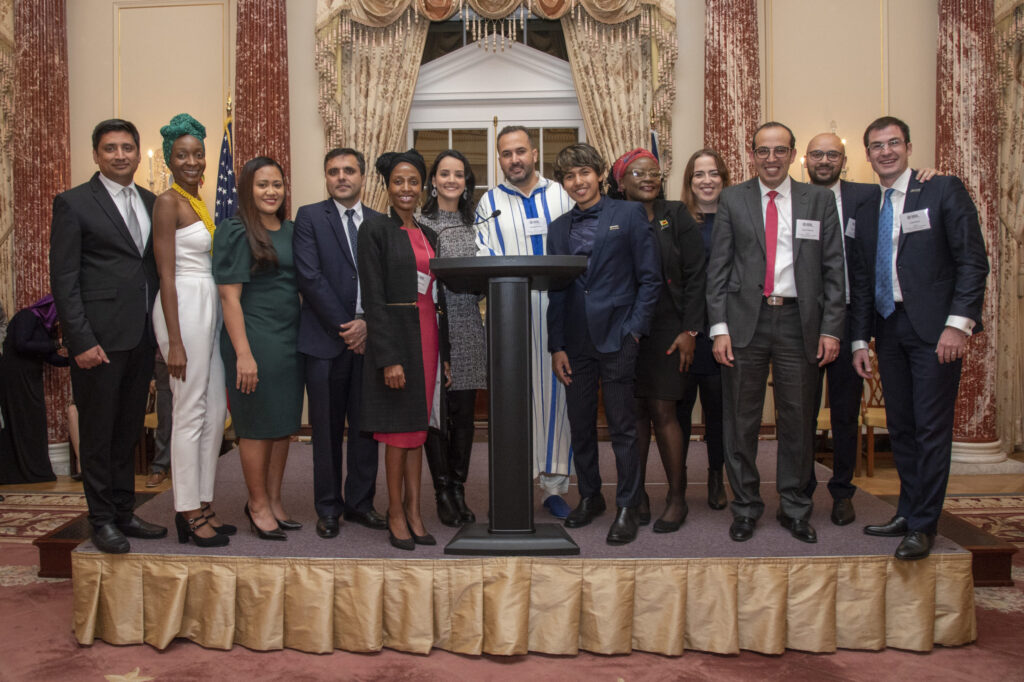 Hubert H. Humphrey Fellows at 2018 Global Leadership Forum Diplomatic Reception, standing on a small raised platform with a podium in front of them.