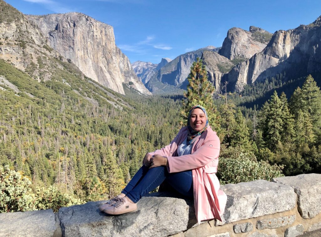 Woman in pink jacket and hijab sitting in front of a mountain at a national park