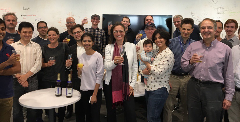 A large gathering of people holding drinks and smiling at the camera, with Sophie Vandebroek in the center raising a glass of champagne.