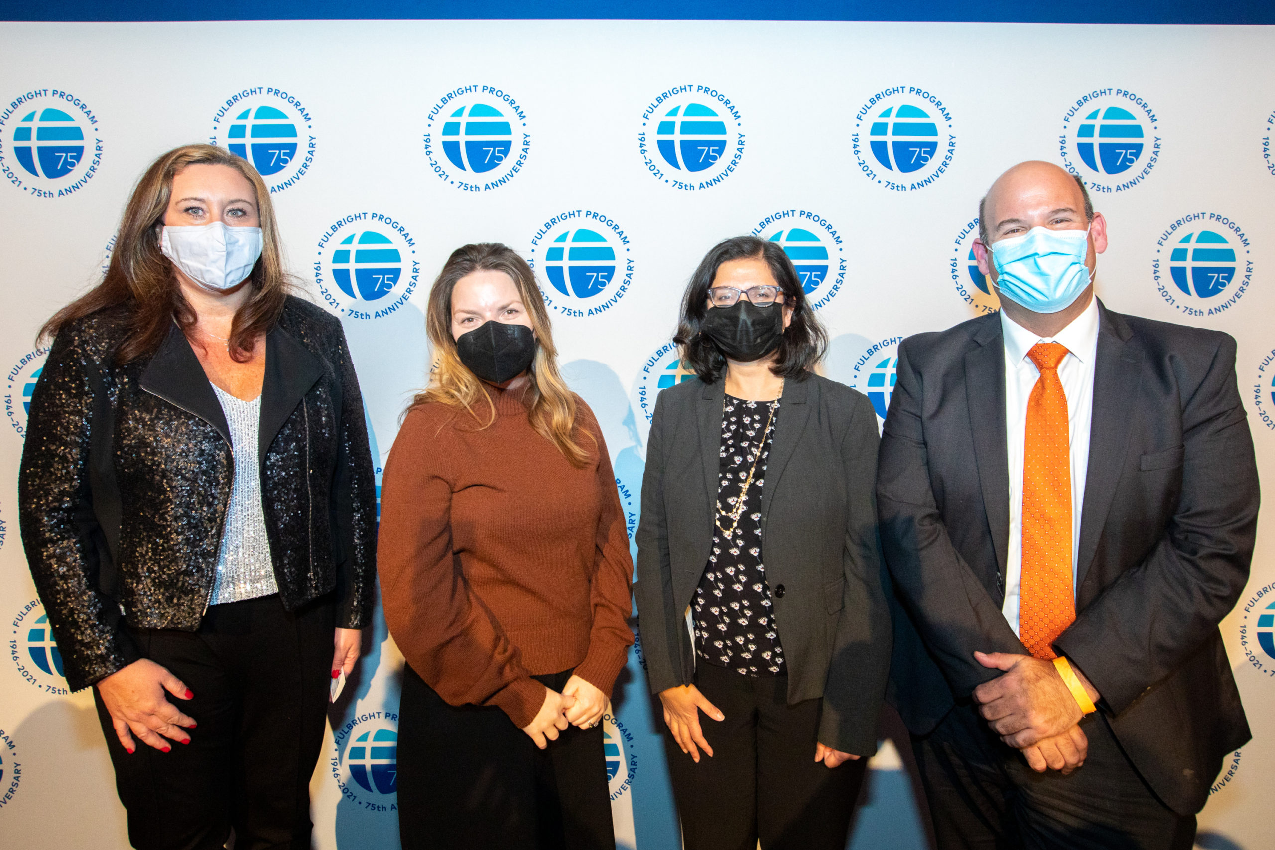 Group of people standing in front of a backdrop of the Fulbright logo. All are wearing business attire and wearing masks.