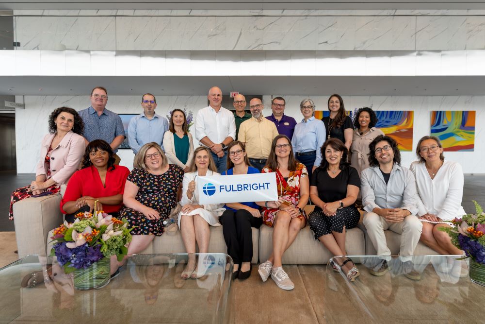 Group of Fulbright Advisers sitting on bench together holding Fulbright sign. 