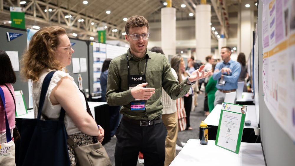 Two people standing next to NAFSA poster talking