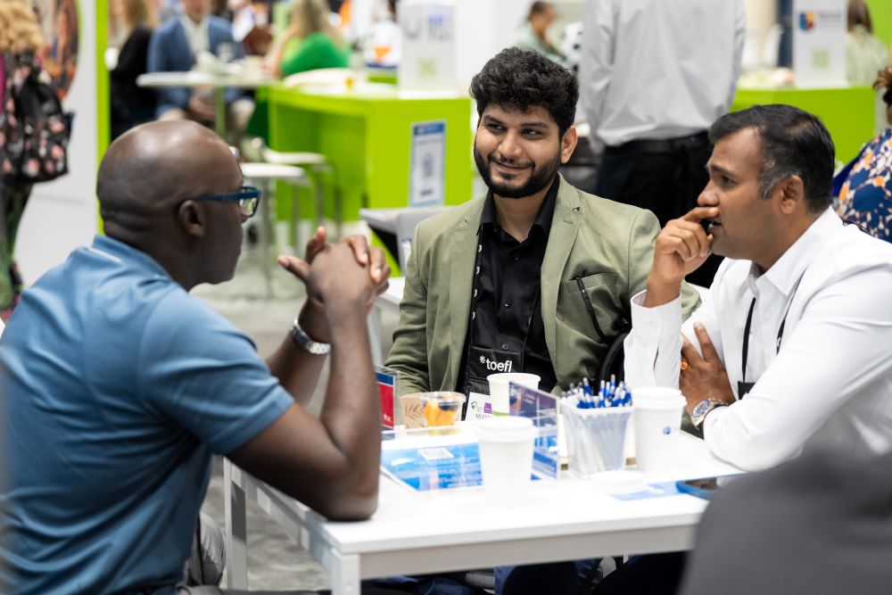 Three people sitting around white table in discussion at NAFSA