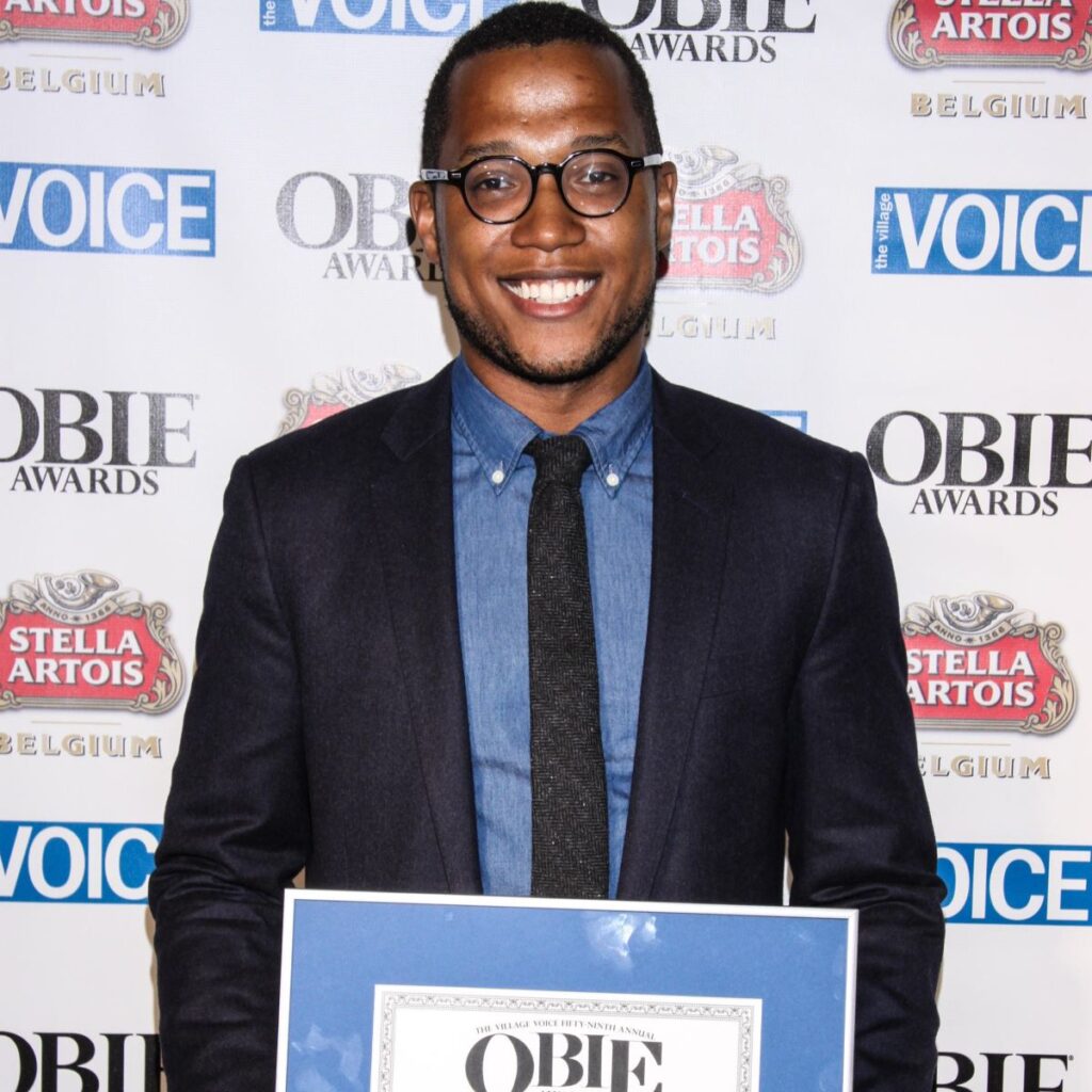 Branden Jacobs-Jenkins standing in front of step and repeat sign holding OBIE award