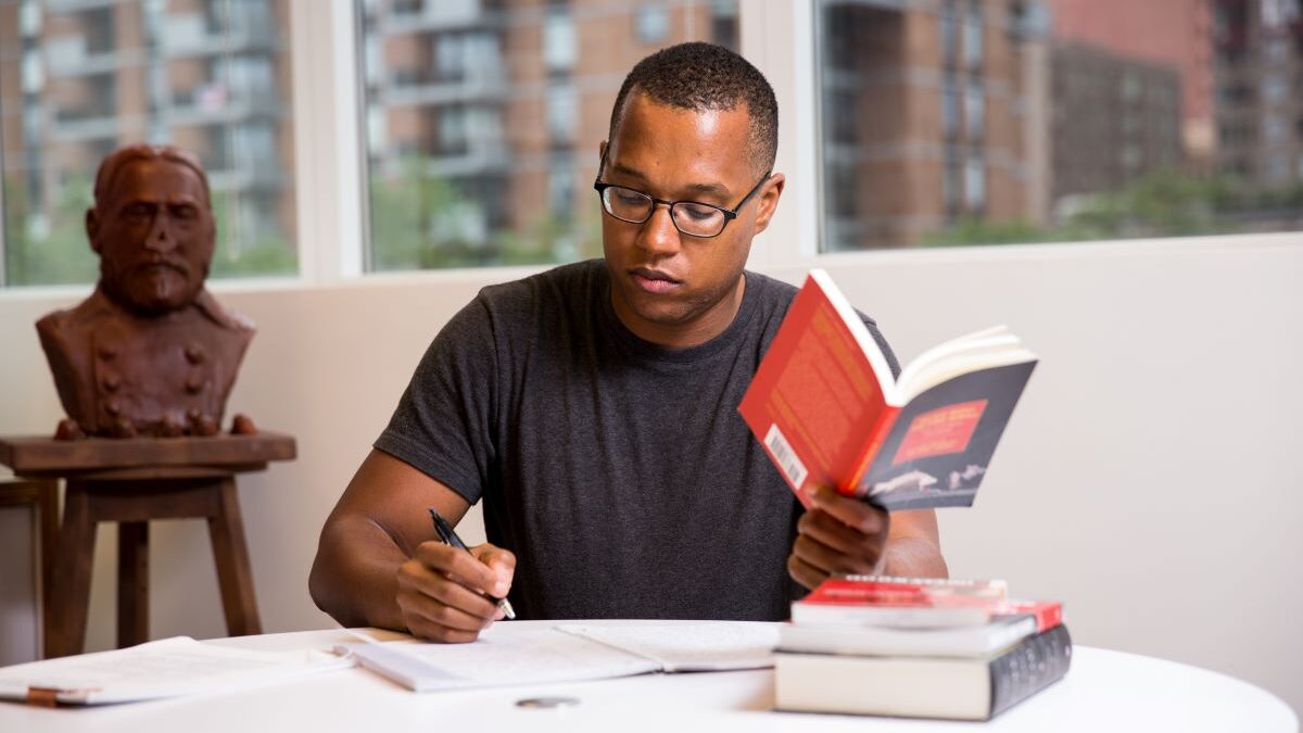 Branden Jacobs-Jenkins sitting at table holding book while writing on page
