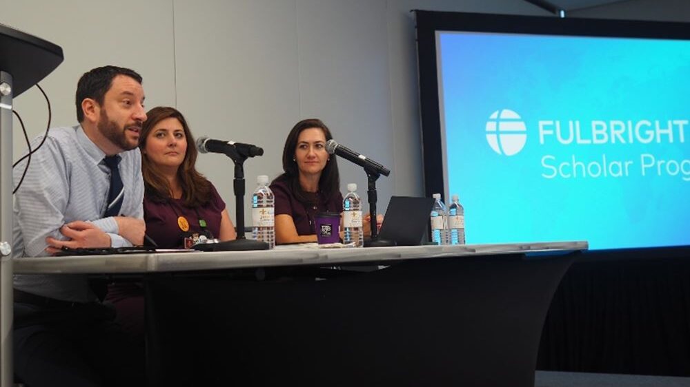 Three people sitting at table next to projector screen speaking on NAFSA panel 