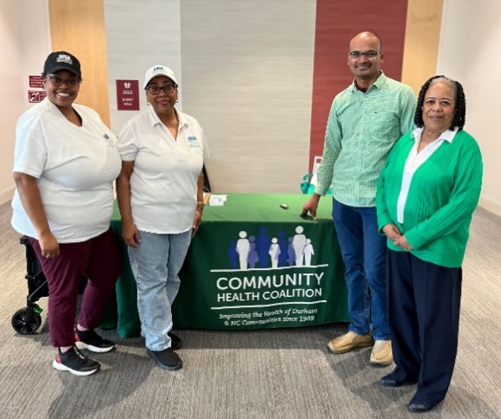 Dr. Karuppusamy standing in front of booth table with members of Community Health Colition