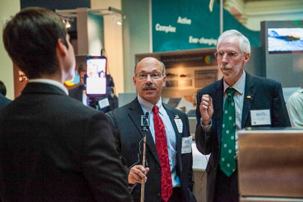 Dr. Michael Sfraga holding a stick talking to two other people