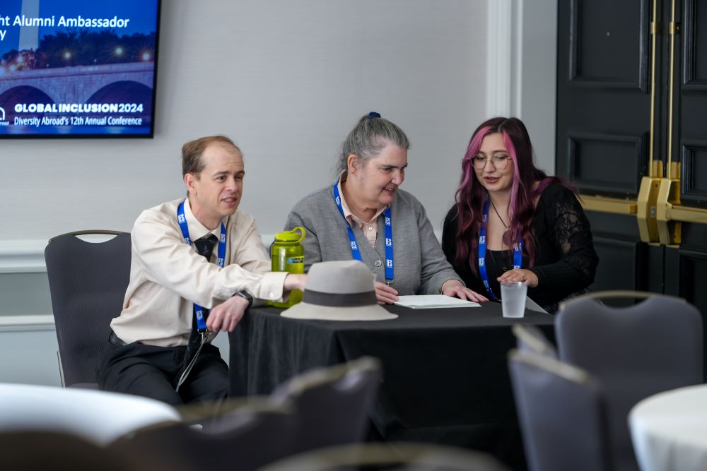 Moira Egan sat at table chatting with two other presenters at conference presentation. 