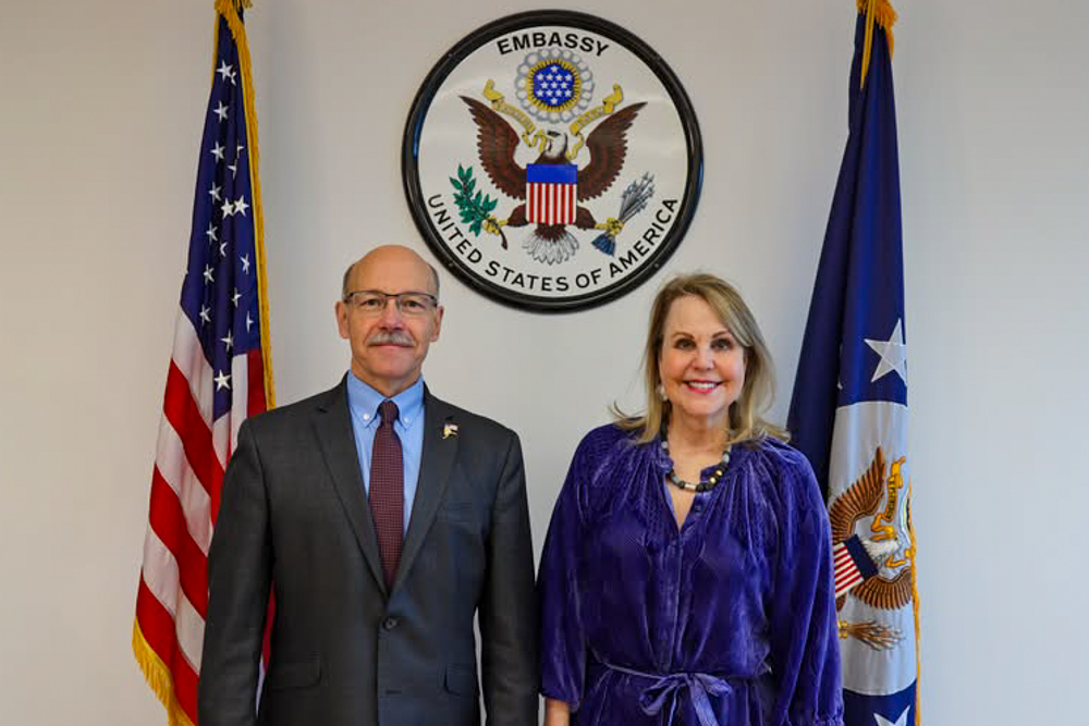 Dr. Michael Sfraga at Iceland Embassy standing with official in front Embassy Seal and flags