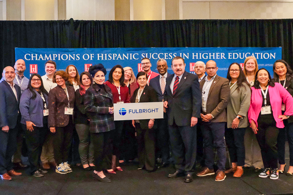 A group of people posing on stage at HACU Conference with a "FULBRIGHT" sign in front of a banner reading "CHAMPIONS OF HISPANIC SUCCESS IN HIGHER EDUCATION."