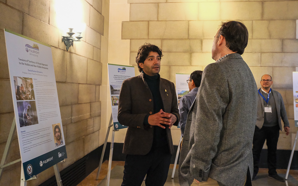 Two men conversing at a poster session, with informational displays in the background.