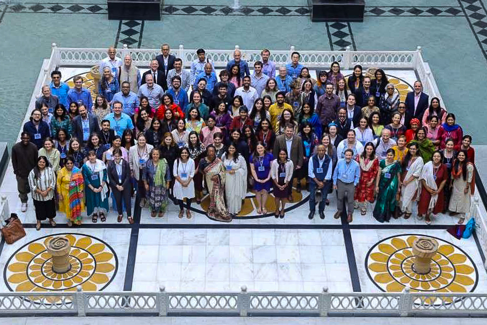 A large diverse group of people posing in a courtyard with a patterned marble floor at Conference