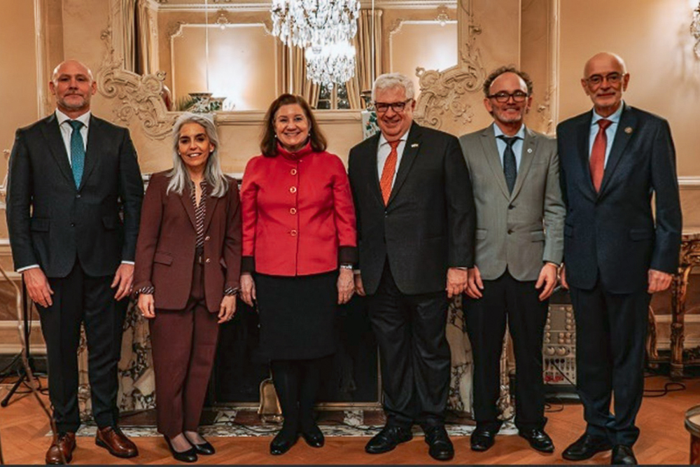 A group of six people in professional attire standing in an ornate room with a chandelier.