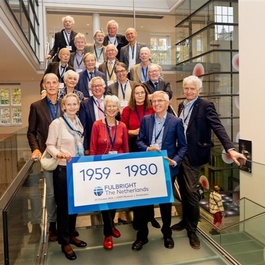 A group of people on a staircase holding a sign that reads "1959 - 1980 Fulbright The Netherlands."