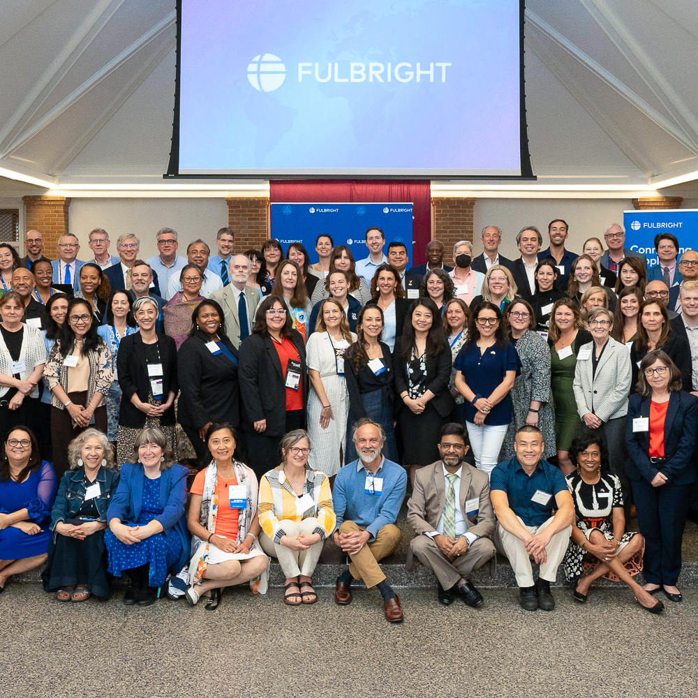 A group photo of diverse people in formal attire with "FULBRIGHT" displayed in the background.