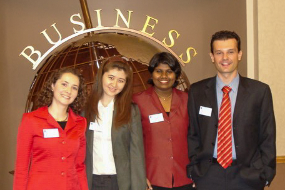 Four people posing in front of a globe structure with "BUSINESS" above them, dressed in professional attire.