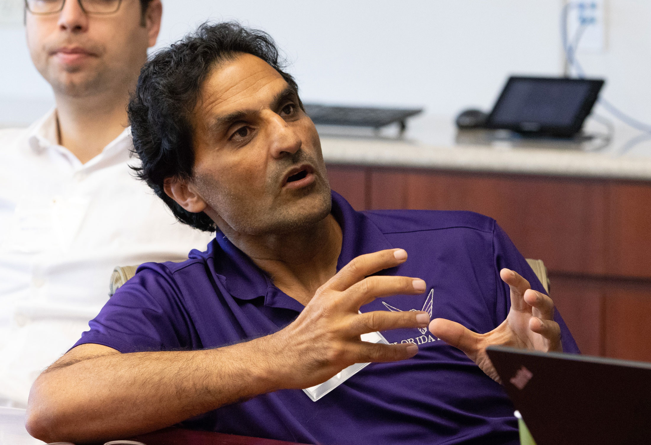 Dr. Razan in a purple polo shirt speaks animatedly with hands gesturing.