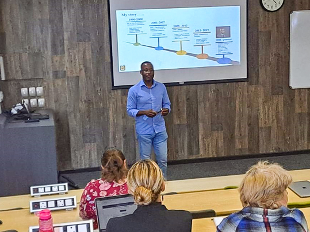 Wilson Majee presenting a timeline on a screen in a lecture hall with a small audience.