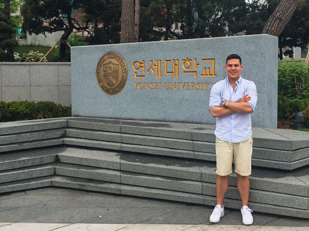 Benjamin Rich standing in front of a Yonsei University sign with gold lettering and a round seal.