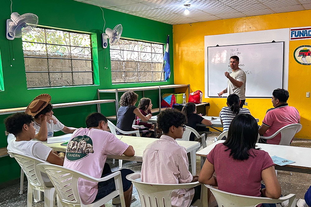 Classroom scene with students and a teacher at a whiteboard in a colorful room.