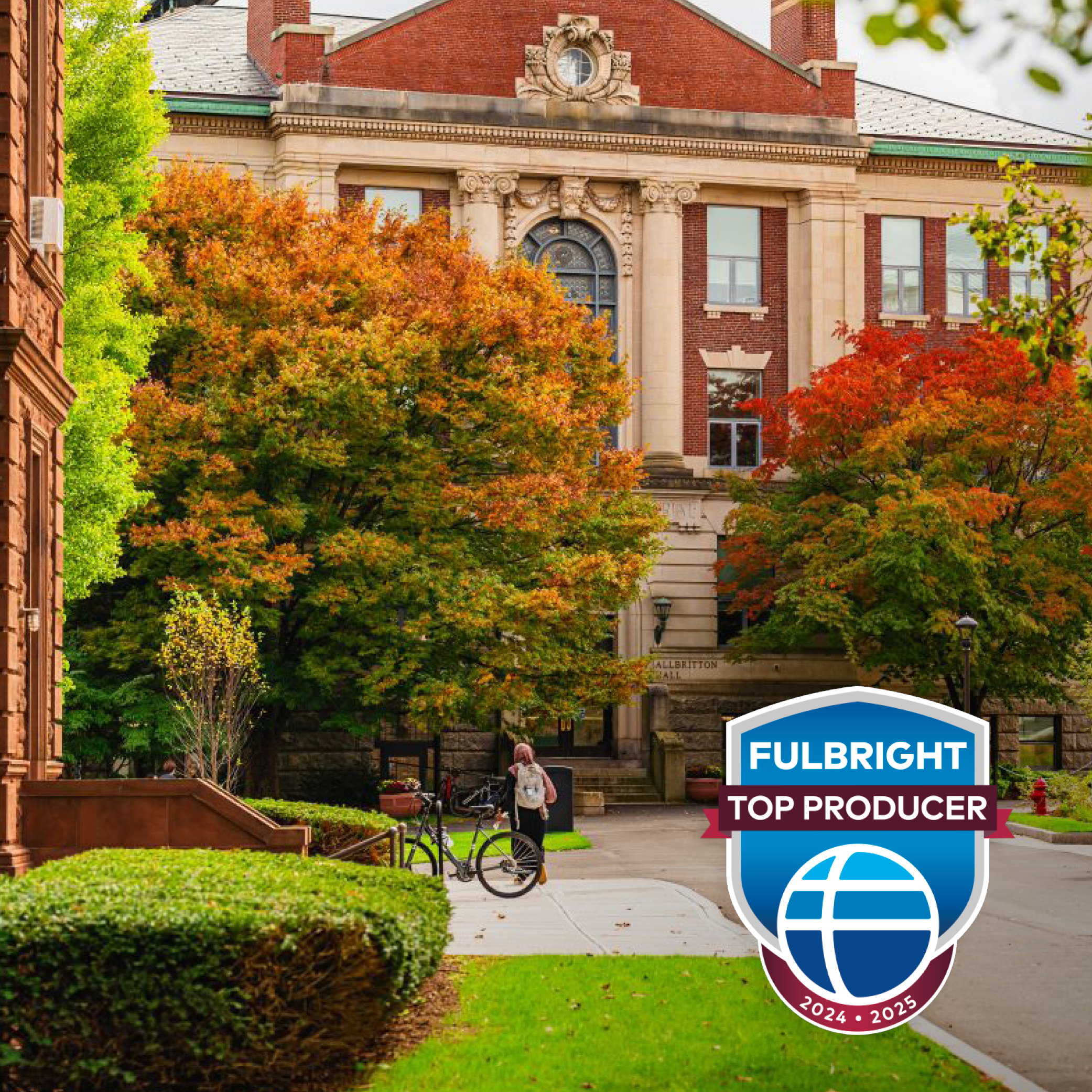 A red brick academic building with autumn trees and a "FULBRIGHT TOP PRODUCER 2024-2025" badge.