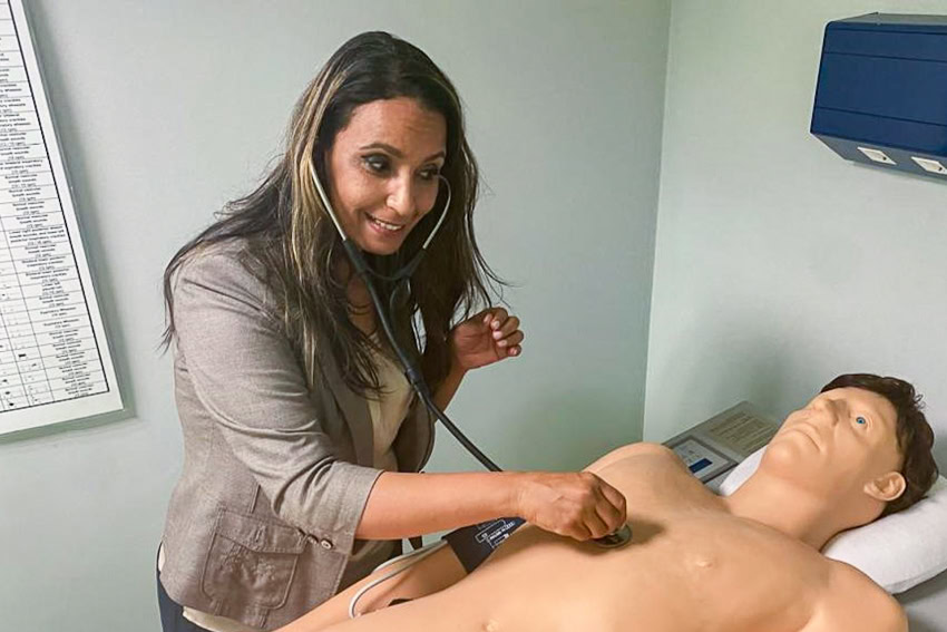 Woman examines a medical mannequin with a stethoscope in a clinical setting.