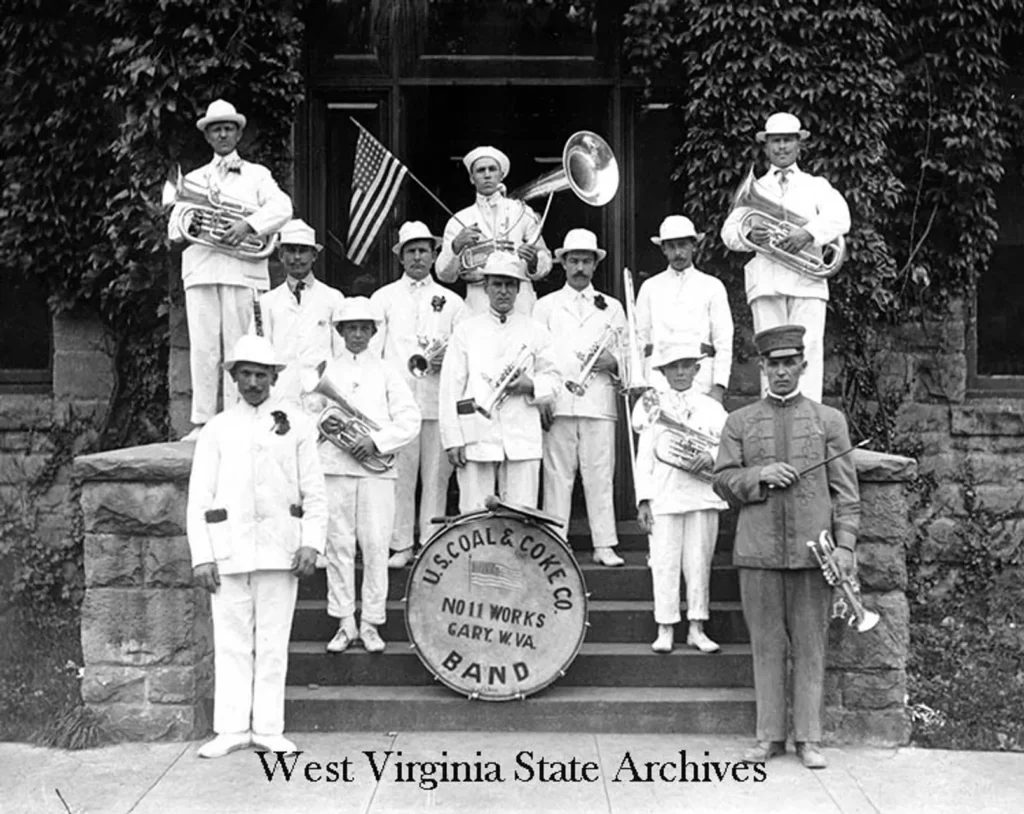 A historical marching band in white uniforms poses with instruments on stone steps.