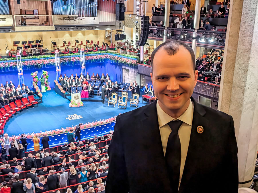 Downey wearing suit inside auditorium at Nobel Prize ceremony with people on stage