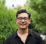 Person wearing glasses and a black shirt standing in a garden with green foliage.