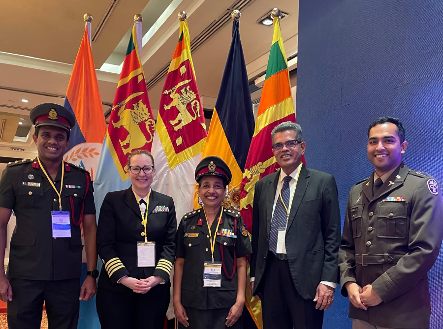 Dr. Worlton standing in front of flags wearing uniform with four men who are members of U.S. and Sri Lanka military
