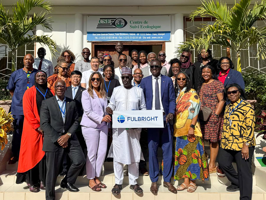A group of twenty-three people poses on steps in front of a building, holding a "FULBRIGHT" sign.