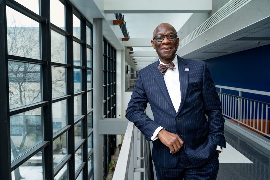Oscar Barton, Jr. in a pinstripe suit and bow tie standing in a modern hallway with large windows.