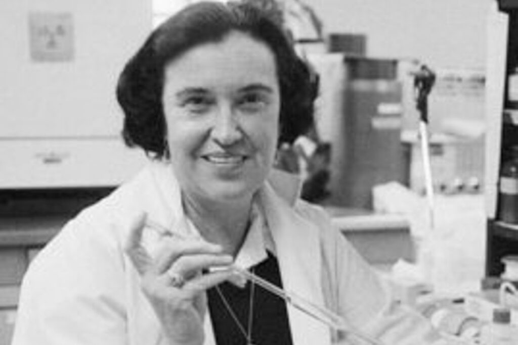 Rosalyn Yalow holding a pipette in a lab and wearing a white lab coat with equipment surrounding her
