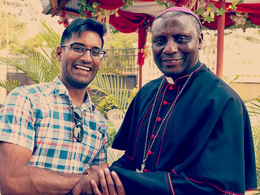 Reddi in plaid shirt standing next to a man in clerical attire shaking hands in an outdoor setting