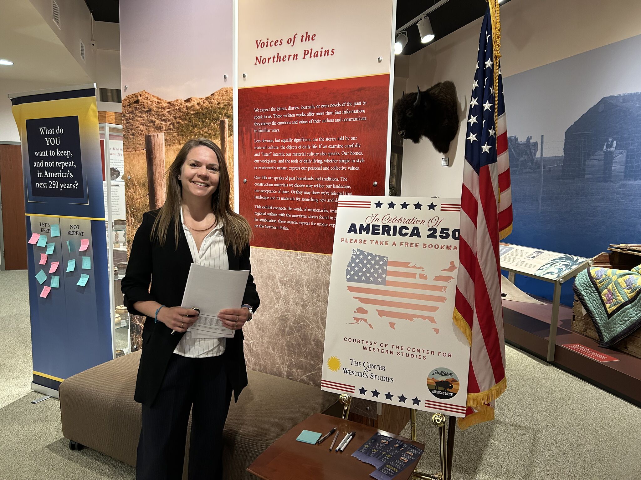 Visiting scholar at American Heritage exhibit with American flag and informational displays.