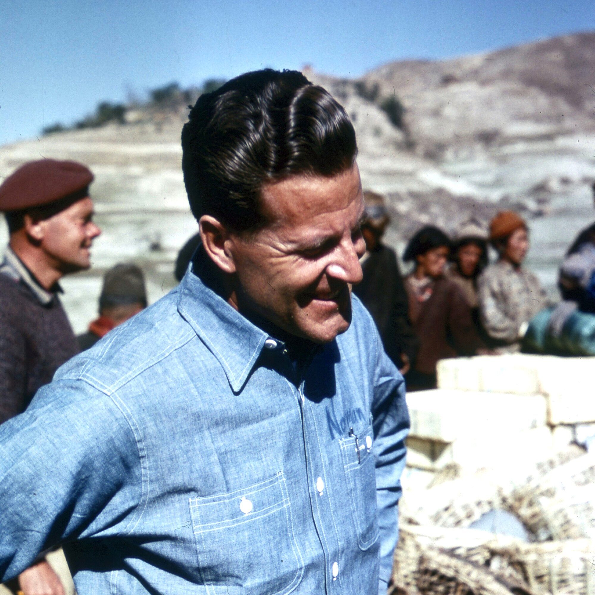 Man in blue shirt standing with baskets and gear at a base camp on Mt. Everest