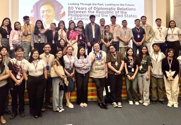 A large group of students and scholars at the front of an auditorium in front of a screen showing text about diplomatic relations between the U.S. and the Philippines