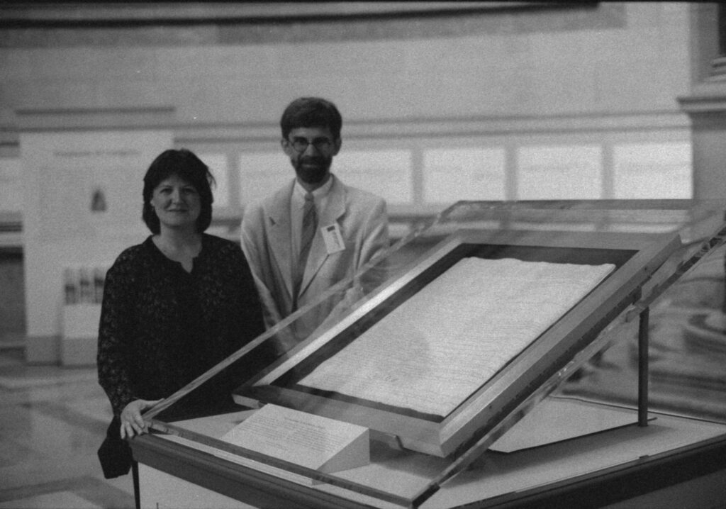 A man and a woman standing behind a display case containing a historic parchment document under glass