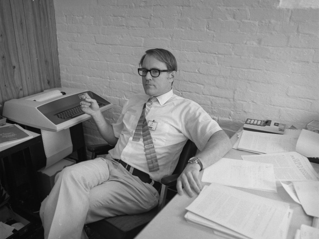 Man wearing glasses sitting in 1960s office with terminal on his desk, wtihout a display screen