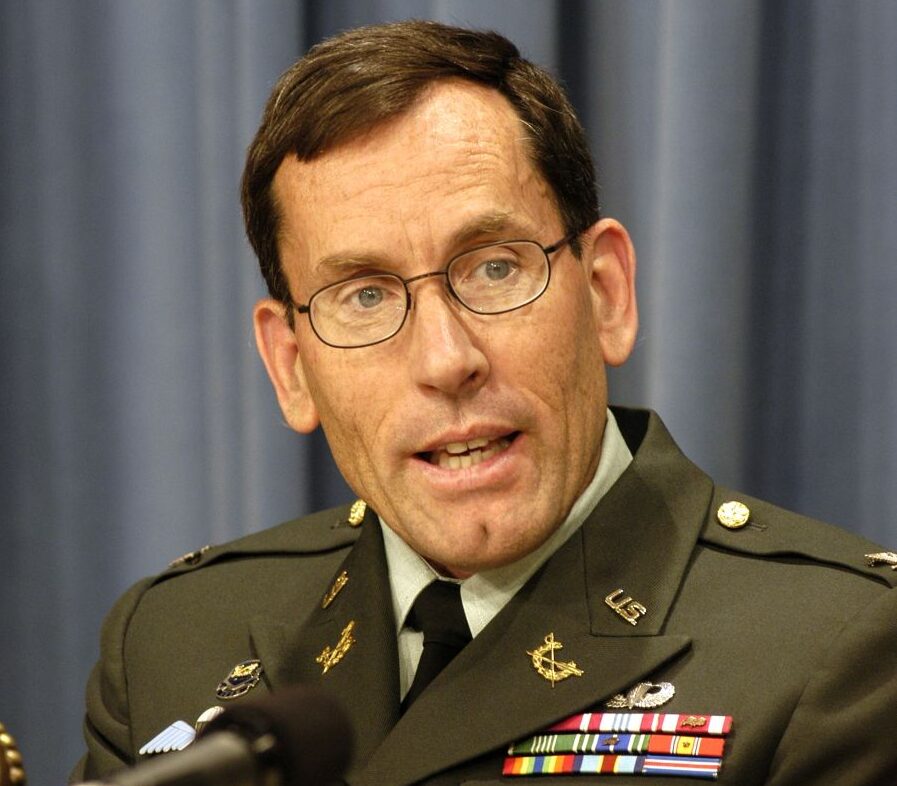 Man wearing formal Army uniform with medals and ribbons , sitting in front of a microphone