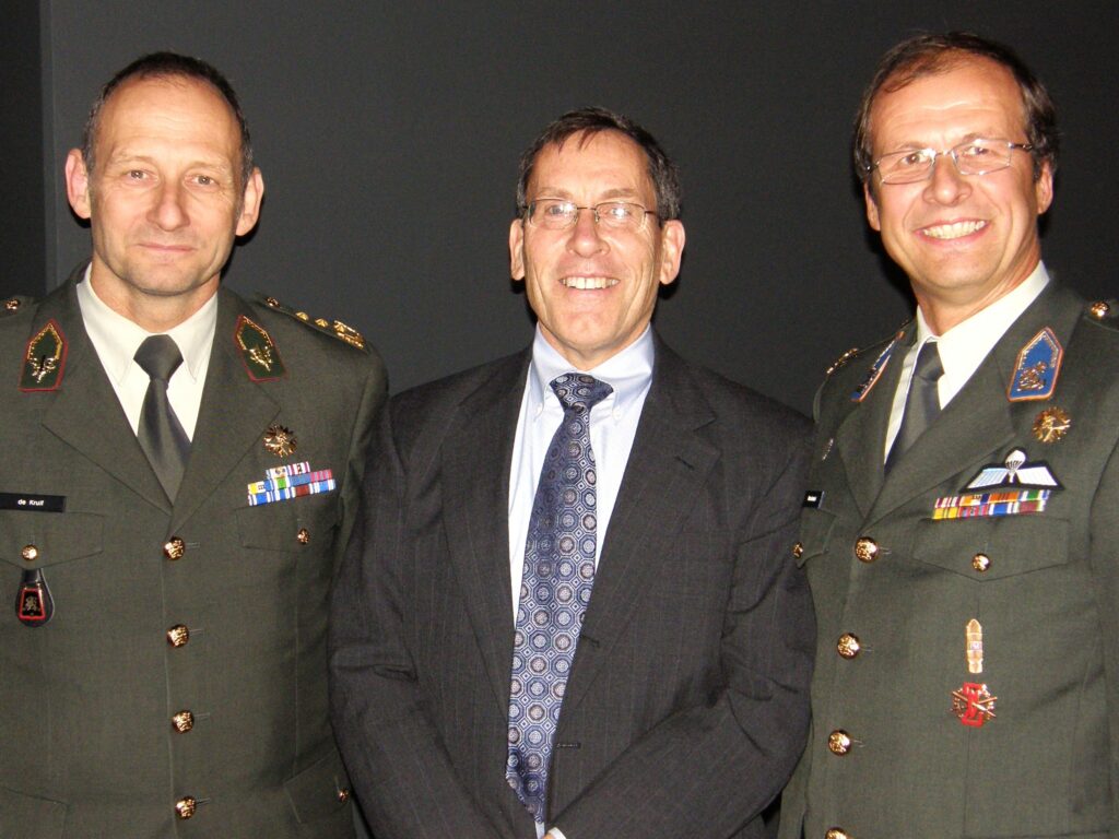 man wearing civilian suit and tie standing between two men in Dutch military uniforms