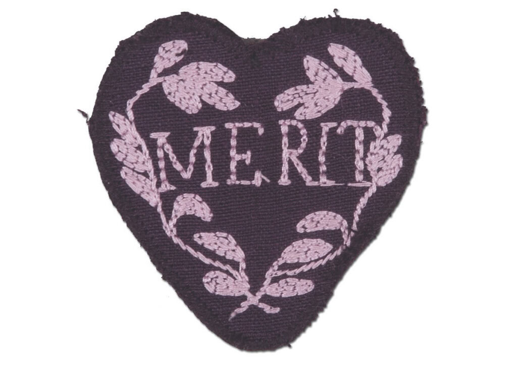 Purple colored cloth patch in the shape of a heart embroidered with the word MERIT surrounded by two leafy branches in a curved wreath-like shape 
