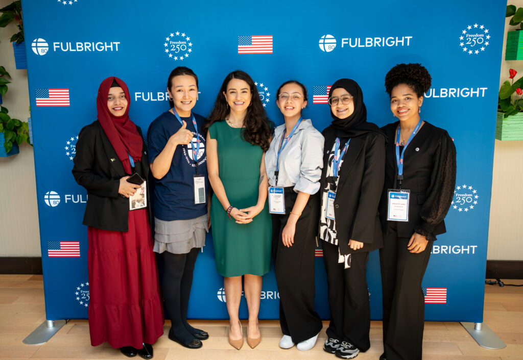 six women standing in front of blue background with Fulbright logo and American Flag and Freedom 250 logo