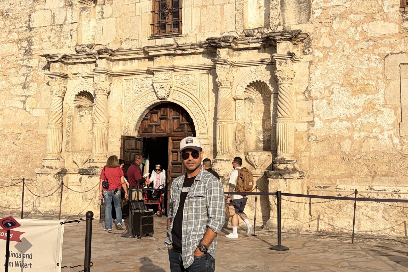 Man standing in front of Spanish-style mission building from 1700s with limestone and adobe walls and large wooden doors made from timber