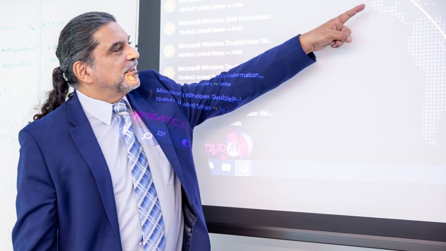 Man wearing blue suit and tie standing in front of digital whiteboard pointing at image on screen