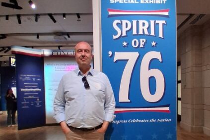 Man standing in front of a red, white and blue banner that says Spirit of '76